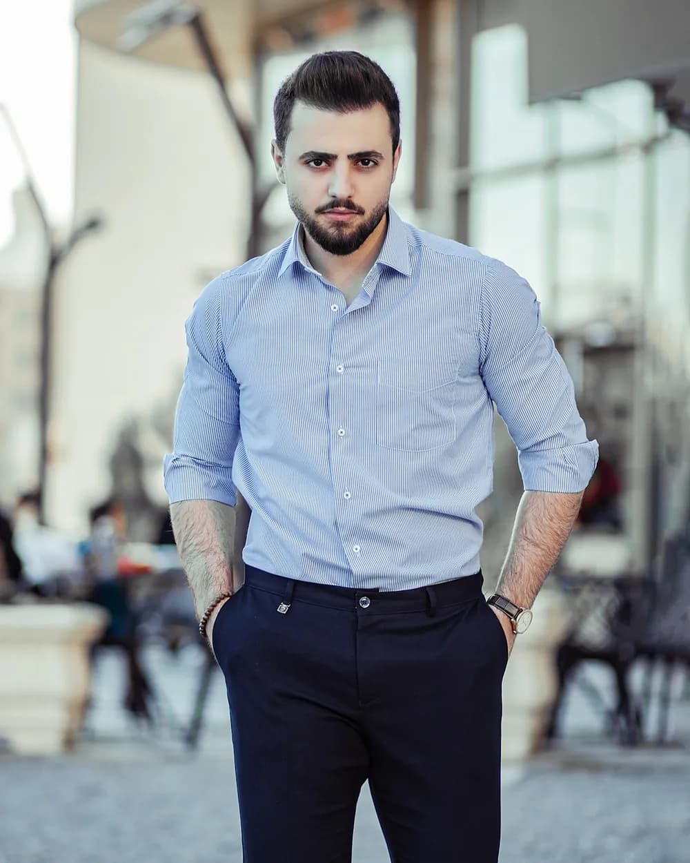 A man in a light blue oxford shirt and navy trousers